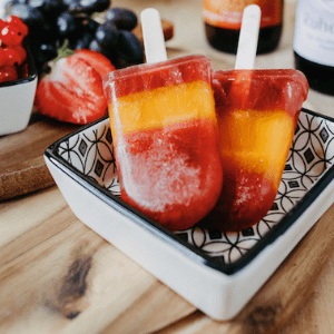 Eis aus Saft serviert in einer Schüssel auf einem Holztisch mit frischem Obst und Flaschen im Hintergrund