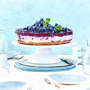 Heidelbeer-Frischkäse-Torte auf einer Tortenplatte mit blauem Tischgedeck