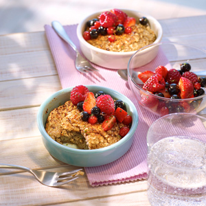 Porridge mit Beeren in blauen Schalen mit Gabel und Obst in einer Glasschale mit einem Glas Wasser auf einem rosa Geschirrtuch