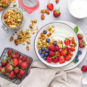 Serviervorschlag Granola mit Joghurt, Heidelbeeren, Himbeeren und Erdbeeren auf einem Teller